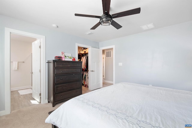 bedroom with light carpet, visible vents, baseboards, a walk in closet, and a closet