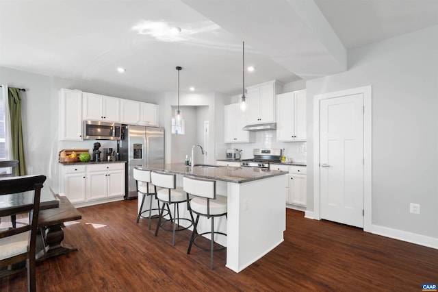 kitchen with white cabinets, appliances with stainless steel finishes, a kitchen island with sink, under cabinet range hood, and a sink