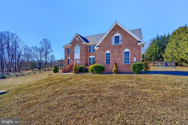 view of front of house featuring a trampoline, a front lawn, and brick siding