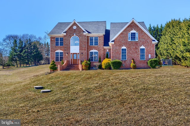 view of front of home featuring a front yard, a trampoline, and brick siding