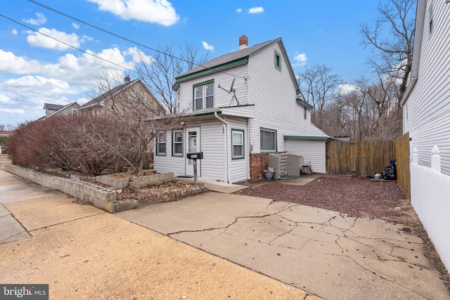 exterior space featuring concrete driveway, a chimney, and fence