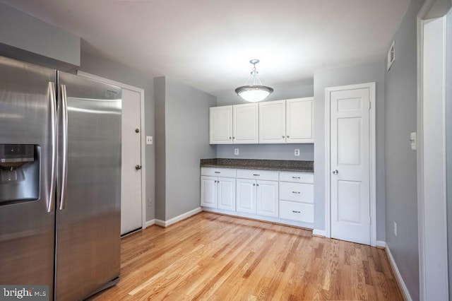 kitchen featuring stainless steel fridge with ice dispenser, hanging light fixtures, light wood-style flooring, white cabinets, and baseboards