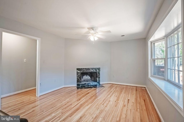 unfurnished living room featuring a ceiling fan, a high end fireplace, baseboards, and wood finished floors