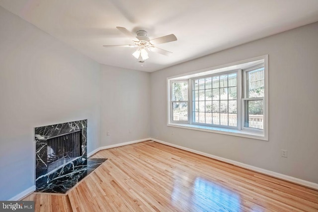 unfurnished living room featuring a ceiling fan, a fireplace, baseboards, and wood finished floors