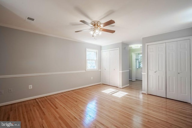 unfurnished bedroom with two closets, visible vents, light wood-style floors, ornamental molding, and baseboards