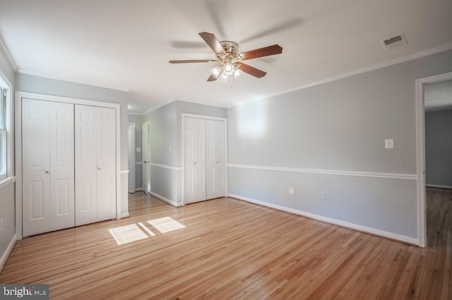 unfurnished bedroom featuring baseboards, visible vents, two closets, and wood finished floors