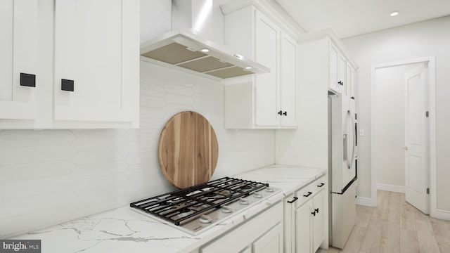 kitchen with light stone counters, white cabinetry, and wall chimney range hood