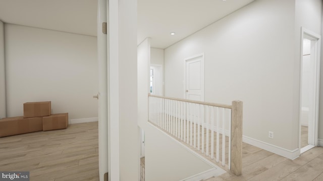 hallway featuring light wood-style floors, baseboards, and an upstairs landing