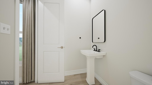 half bath featuring baseboards, toilet, and wood finished floors