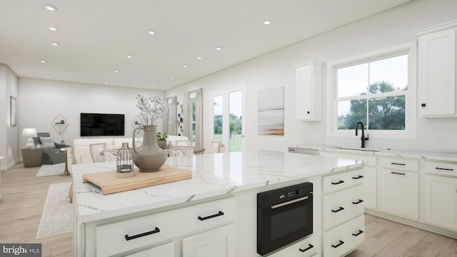 kitchen with light stone counters, white cabinetry, a sink, black oven, and plenty of natural light