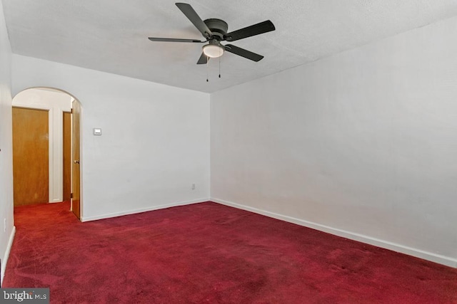 carpeted empty room featuring a ceiling fan, arched walkways, and baseboards