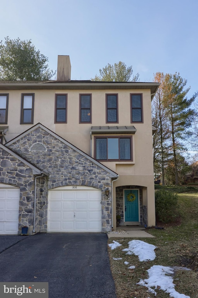 view of property with aphalt driveway, a garage, stone siding, stucco siding, and a chimney