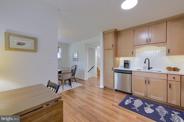 kitchen featuring tasteful backsplash, dishwasher, light countertops, light wood-type flooring, and a sink