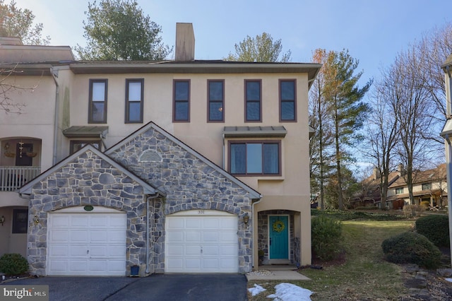 view of property with a garage, driveway, a chimney, and stucco siding