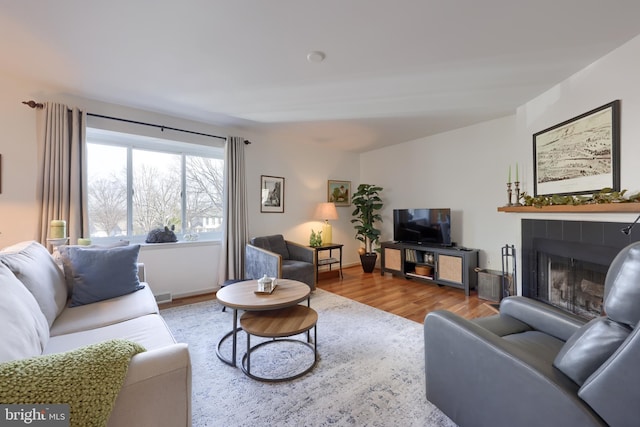 living area featuring a tile fireplace, baseboards, and wood finished floors