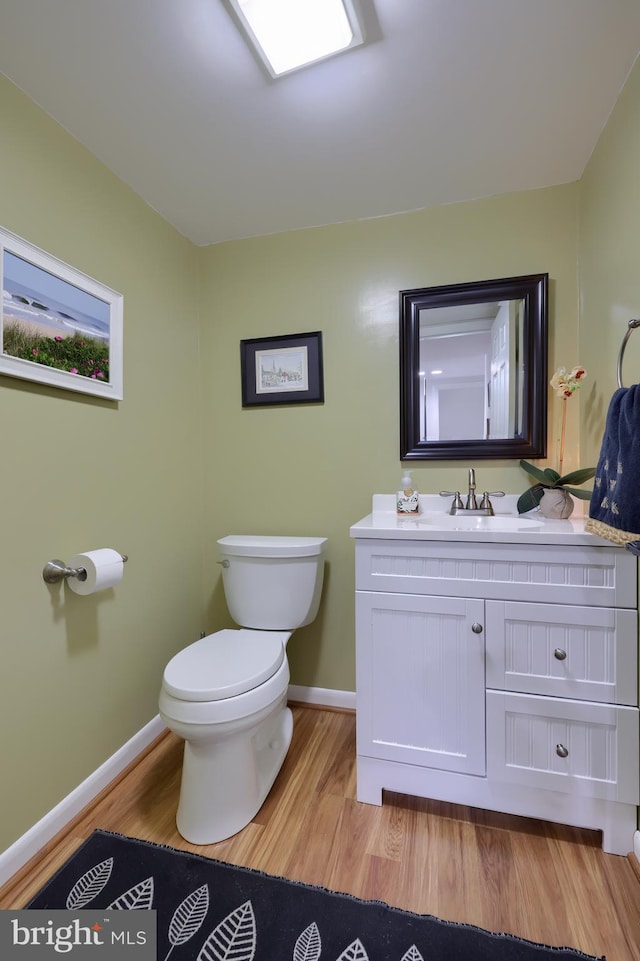 half bathroom with vanity, wood finished floors, toilet, and baseboards