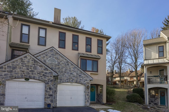 view of property featuring aphalt driveway, a chimney, an attached garage, and stucco siding