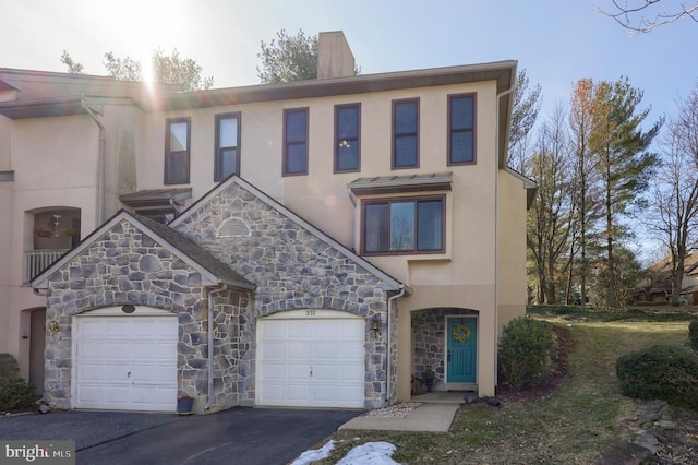 townhome / multi-family property featuring a garage, stone siding, driveway, and stucco siding