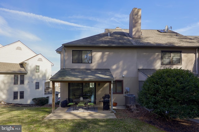 back of house featuring a patio, a chimney, stucco siding, a lawn, and central AC unit