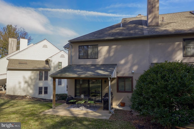 rear view of house featuring a patio, a yard, roof with shingles, stucco siding, and a chimney