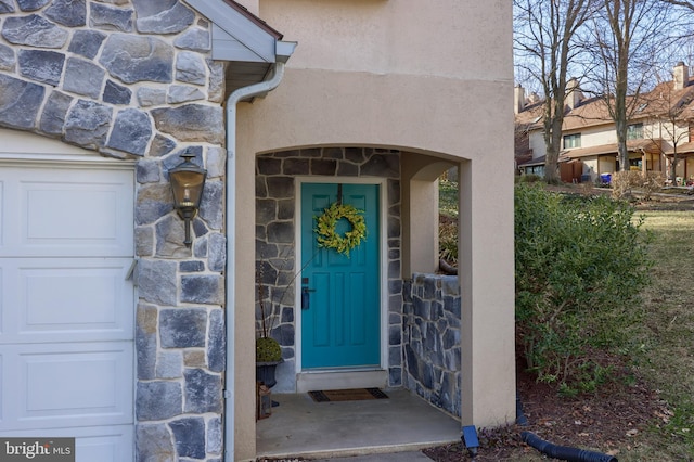 entrance to property featuring a garage, stone siding, and stucco siding