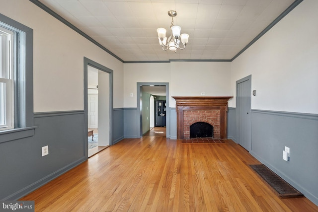 unfurnished living room with a wainscoted wall, a fireplace, visible vents, light wood-type flooring, and crown molding