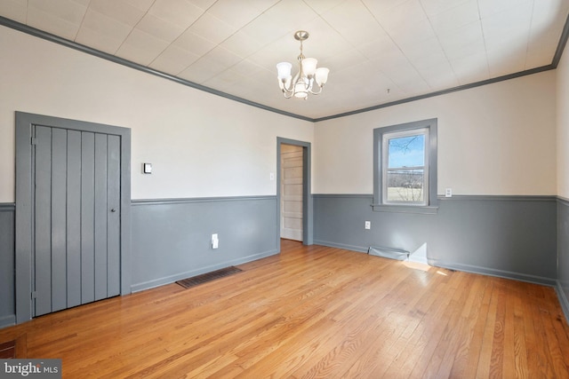 empty room with ornamental molding, wood-type flooring, wainscoting, and an inviting chandelier