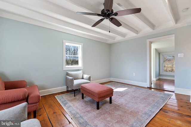 living area featuring hardwood / wood-style floors, a ceiling fan, baseboards, and beam ceiling