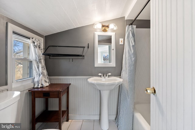 full bath with a wainscoted wall, toilet, vaulted ceiling, a sink, and tile patterned floors