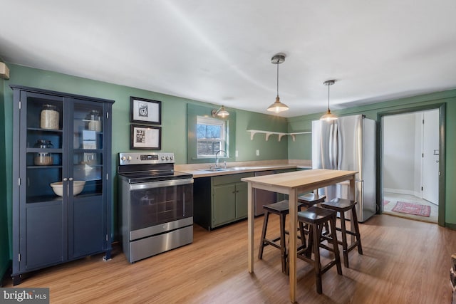 kitchen with decorative light fixtures, stainless steel appliances, light countertops, light wood-style flooring, and a sink