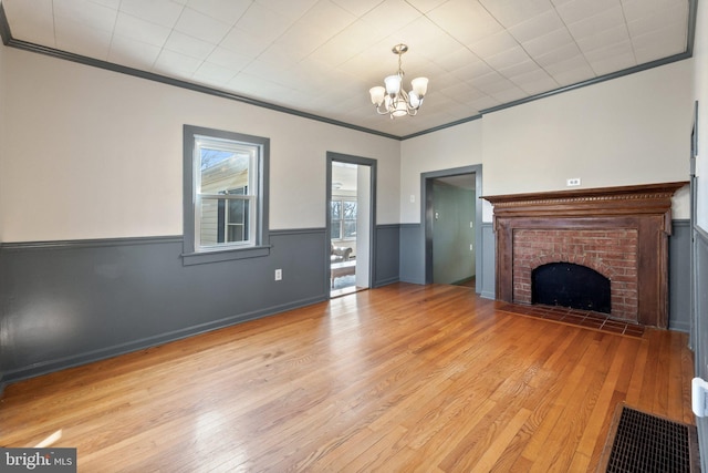 unfurnished living room featuring wainscoting, ornamental molding, a fireplace, and light wood-style flooring