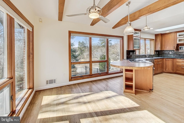 kitchen featuring visible vents, backsplash, glass insert cabinets, a sink, and beamed ceiling