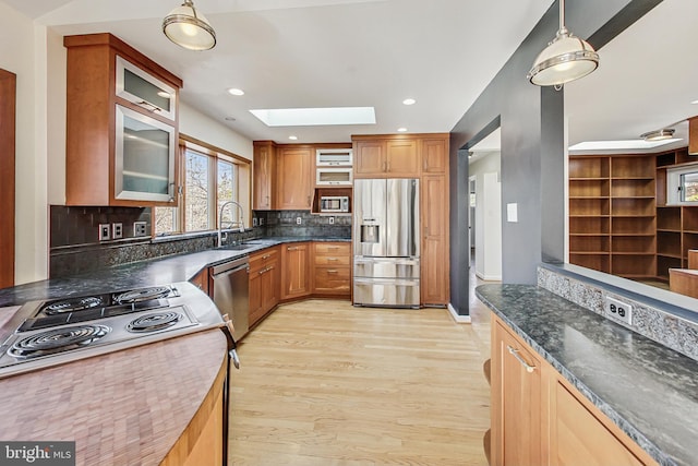 kitchen with a skylight, a sink, light wood-style floors, appliances with stainless steel finishes, and tasteful backsplash