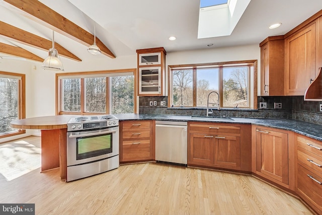 kitchen with a peninsula, a skylight, a sink, appliances with stainless steel finishes, and brown cabinets