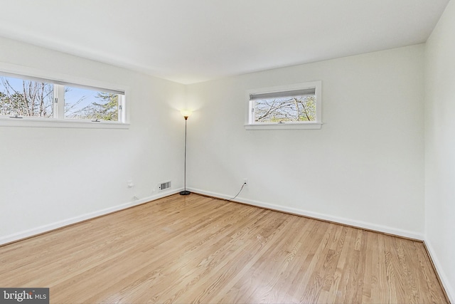 unfurnished room featuring baseboards, wood finished floors, visible vents, and a healthy amount of sunlight