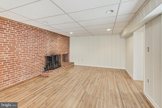 unfurnished living room featuring a paneled ceiling, a brick fireplace, brick wall, wood finished floors, and baseboards