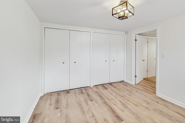 unfurnished bedroom featuring wood finished floors, baseboards, and two closets