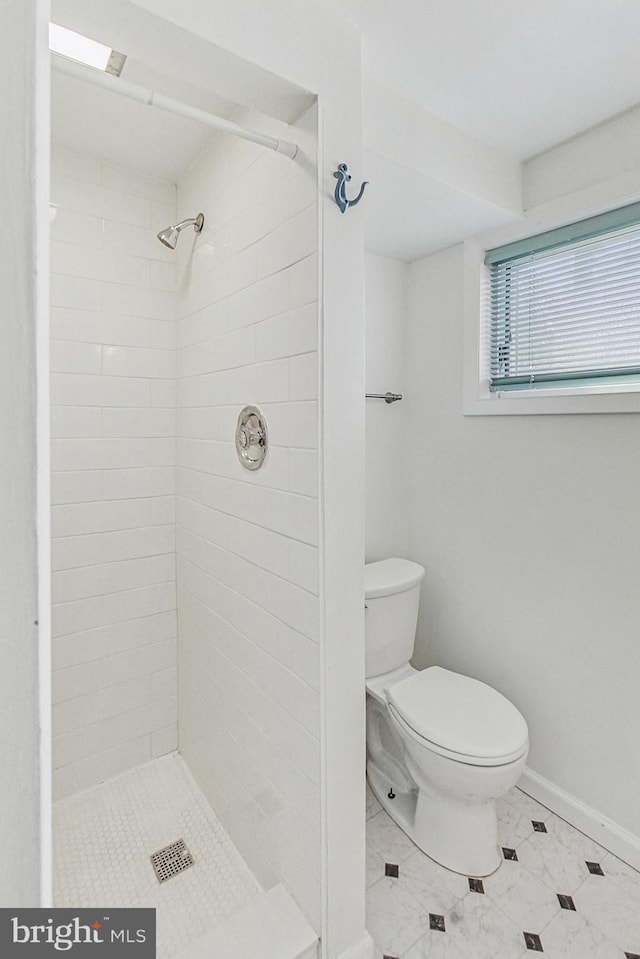 bathroom with a tile shower, toilet, and baseboards