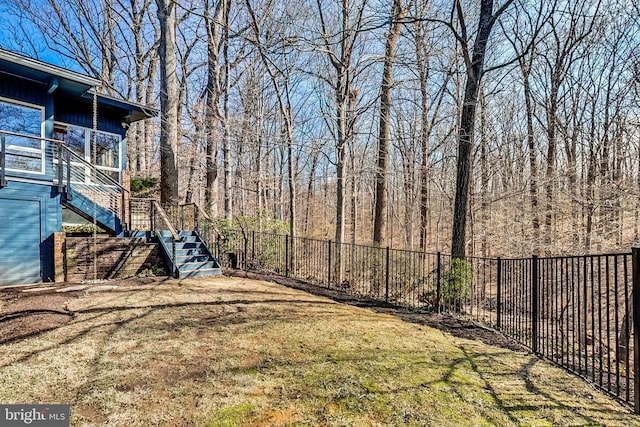 view of yard featuring stairs, fence, and a wooded view