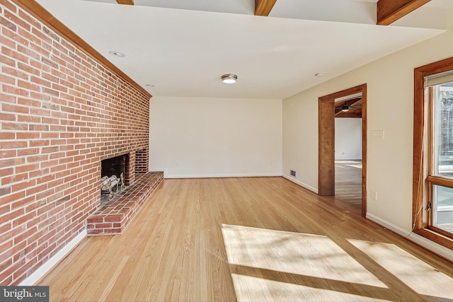 unfurnished living room with visible vents, baseboards, brick wall, wood finished floors, and a brick fireplace