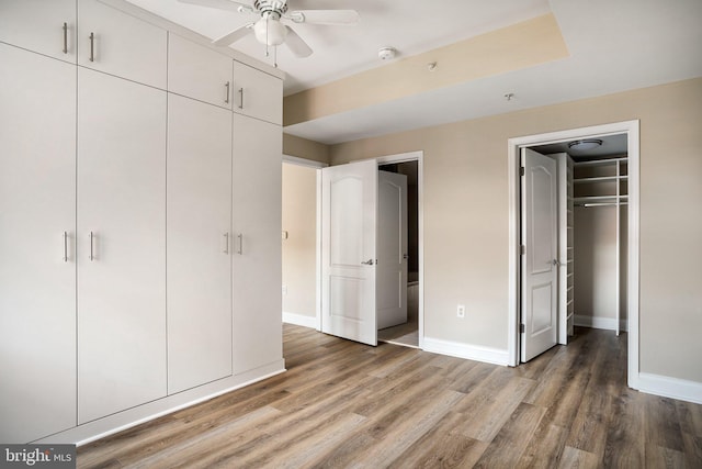 unfurnished bedroom featuring a closet, wood finished floors, a walk in closet, and baseboards