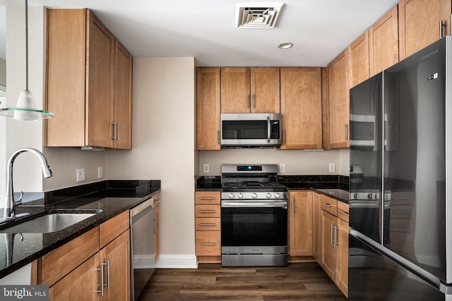 kitchen with dark wood-style flooring, visible vents, appliances with stainless steel finishes, a sink, and dark stone counters