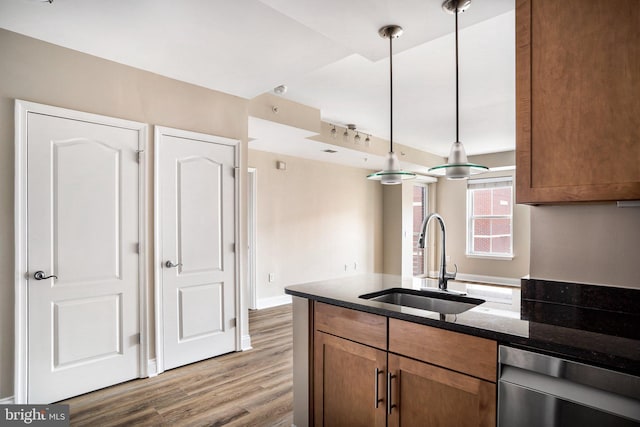 kitchen featuring dark wood-style floors, brown cabinets, decorative light fixtures, stainless steel dishwasher, and a sink