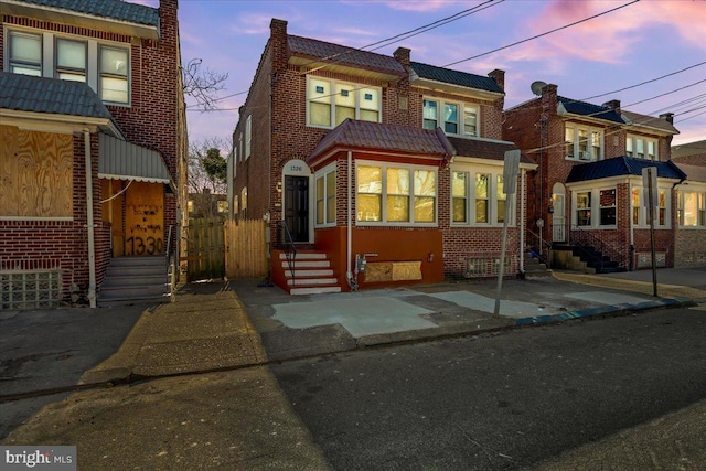 view of front of house with a tile roof, brick siding, and fence