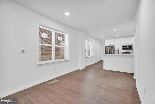 unfurnished living room with dark wood-style flooring, visible vents, and baseboards