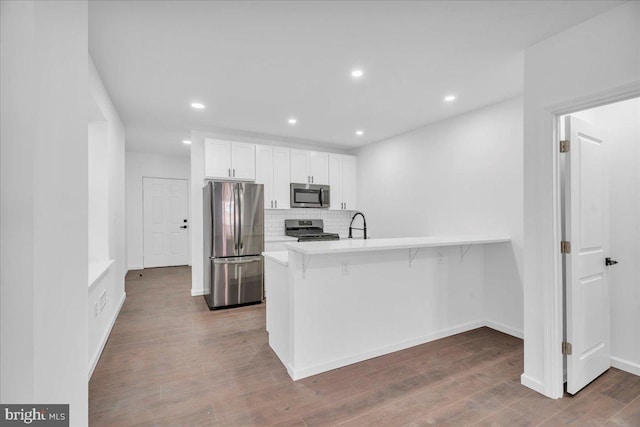 kitchen featuring stainless steel appliances, a peninsula, white cabinetry, a kitchen breakfast bar, and light countertops