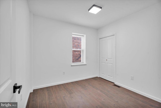 spare room with dark wood finished floors, visible vents, and baseboards