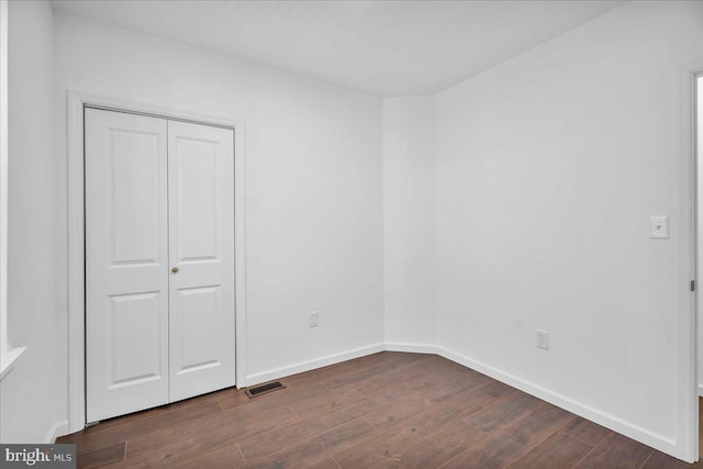 unfurnished bedroom featuring dark wood-style flooring, a closet, visible vents, and baseboards