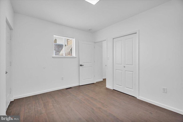 unfurnished bedroom featuring dark wood-style flooring, a closet, visible vents, and baseboards