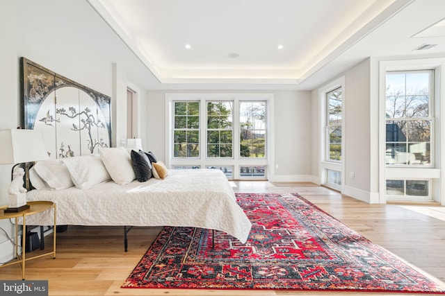 bedroom featuring baseboards, visible vents, a tray ceiling, and wood finished floors